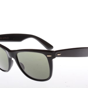 Peut inclure: Lunettes de soleil de style Wayfarer noires avec des verres verts et des accents dor&eacute;s.
