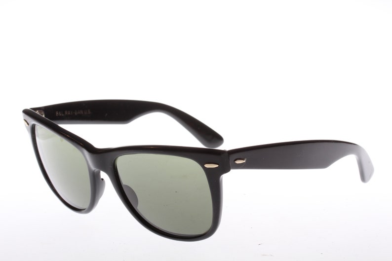 Peut inclure: Lunettes de soleil de style Wayfarer noires avec des verres verts et des accents dor&eacute;s.