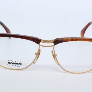 May include: Tortoiseshell eyeglasses with gold metal frames and clear lenses. The brand name "MORWEN" is printed on the left lens.