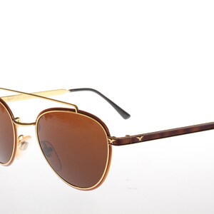 May include: Gold and brown aviator sunglasses with brown lenses. The sunglasses have a gold metal frame and brown plastic arms.