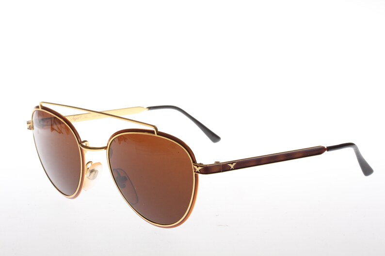 May include: Gold and brown aviator sunglasses with brown lenses. The sunglasses have a gold metal frame and brown plastic arms.