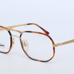 May include: Gold-rimmed glasses with tortoiseshell frames. The glasses have a rectangular shape with slightly rounded edges. The brand name "MORMONT" is visible on the left lens.