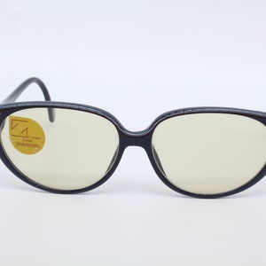 May include: Black cat-eye glasses with a red and blue trim. The lenses are clear and have a yellow sticker that says "Zeiss Unbreakable".