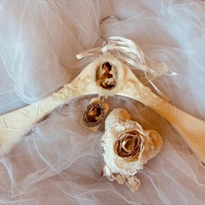 Könnte beinhalten: Elfenbeinfarbener dekorativer Holzkleiderbügel mit floralen und Scroll-Details. Verfügt über ein Porträt im Vintage-Stil in einem ovalen Rahmen und ein passendes Etikett. Eine Stoffblume mit Spitzenakzenten ist ebenfalls vorhanden.