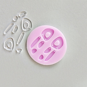 Può includere: Uno stampo in silicone rosa con più forme per realizzare orecchini. Lo stampo ha due forme a goccia grandi, due forme a goccia più piccole e due forme rotonde piccole.