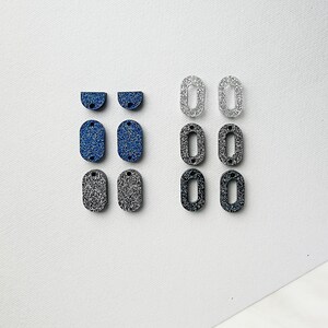 Puede incluir: Surtido de formas de resina cubiertas de purpurina en azul, negro y plateado. Las formas incluyen semic&iacute;rculos, &oacute;valos y rect&aacute;ngulos.