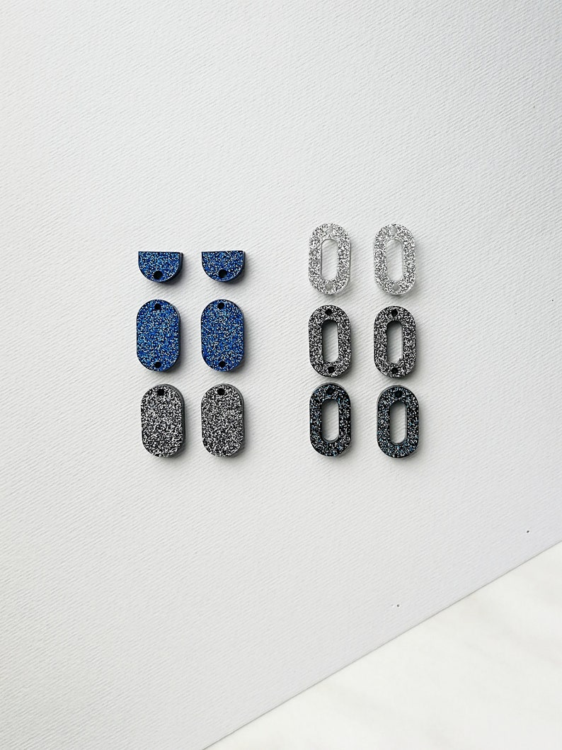 Puede incluir: Surtido de formas de resina cubiertas de purpurina en azul, negro y plateado. Las formas incluyen semic&iacute;rculos, &oacute;valos y rect&aacute;ngulos.