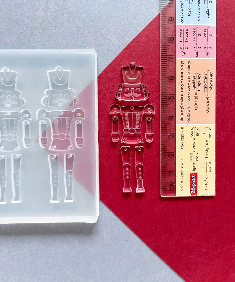 May include: A clear resin mould and a finished resin nutcracker figurine. The mould features two nutcracker shapes, while the figurine stands next to a ruler, approximately 15 cm tall, on a red and grey surface.