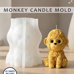 Pode incluir: Um molde de vela de macaco de silicone branco ao lado de uma vela de macaco amarela. A vela de macaco é decorada com padrões semelhantes a rosas. O texto "MONKEY CANDLE MOLD" é exibido acima dos objetos.