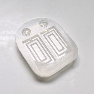 May include: Clear silicone mould for making rectangular earrings with a geometric design. The mould has two earring cavities and two small circles for making earring posts.