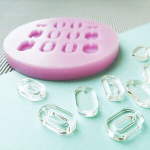 Puede incluir: Un molde de silicona rosa con nueve cavidades ovaladas y un grupo de piezas ovaladas de pl&aacute;stico transparente.