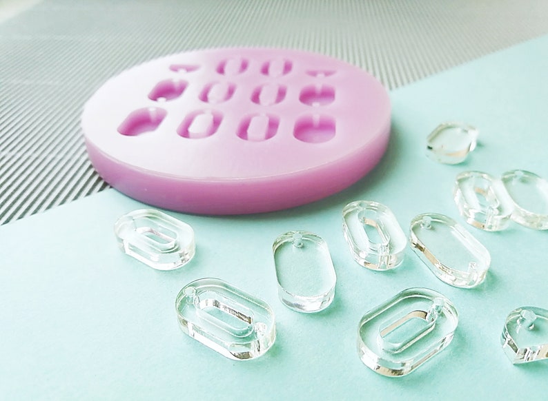 Puede incluir: Un molde de silicona rosa con nueve cavidades ovaladas y un grupo de piezas ovaladas de pl&aacute;stico transparente.