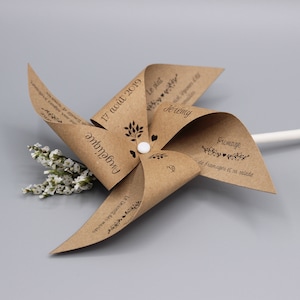 Peut inclure: Un moulin à vent en papier kraft avec le texte "Angélique" et "Jérémy" dessus. Le moulin à vent a également la date "17 août 2019" et les mots "Le plat", "Le dessert des mariés", et "Fromage" dessus.