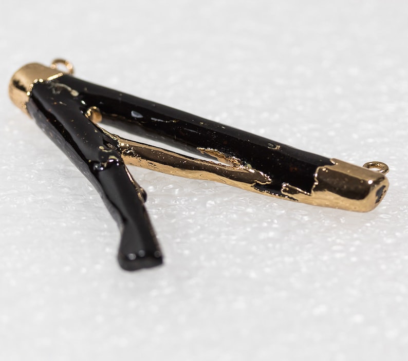May include: Black and gold pendant with a unique, organic shape. The pendant is made of a black material with gold accents. It has a loop at each end for attaching to a chain or cord.