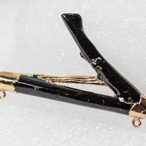 May include: A black twig pendant with gold accents. The twig is shaped like a V and has a gold cap on each end. The pendant is attached to a gold chain.