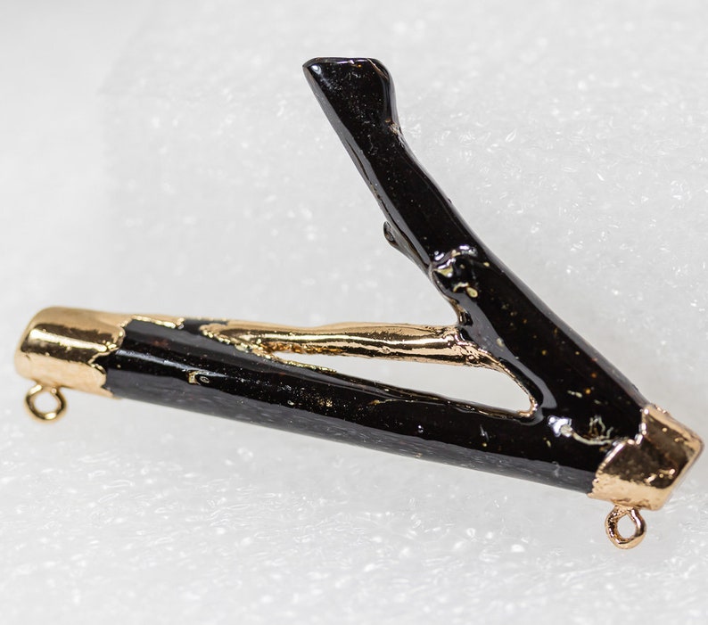 May include: A black twig pendant with gold accents. The twig is shaped like a V and has a gold cap on each end. The pendant is attached to a gold chain.
