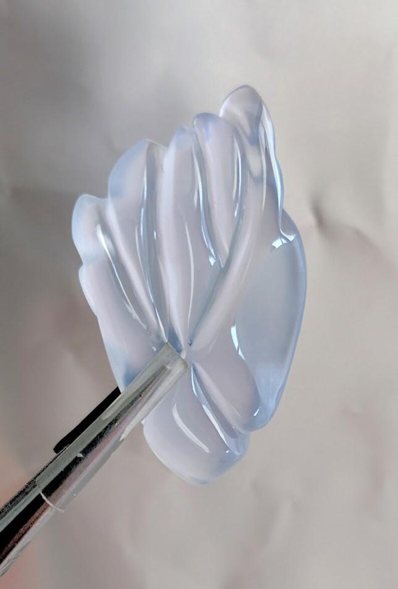 Puede incluir: Un colgante de flor de color azul claro transl&uacute;cido y tallado. La flor tiene un dise&ntilde;o delicado e intrincado con m&uacute;ltiples capas de p&eacute;talos.