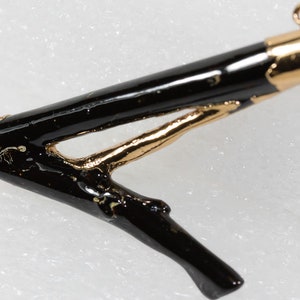 May include: A black and gold twig pendant with a gold loop at the top for hanging. The twig is painted black and has a gold accent on the branch.