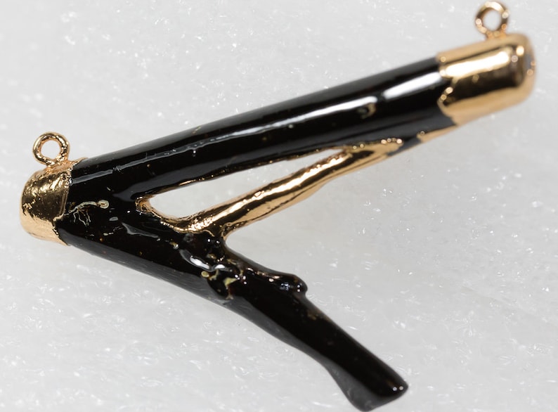 May include: A black and gold twig pendant with a gold loop at the top for hanging. The twig is painted black and has a gold accent on the branch.