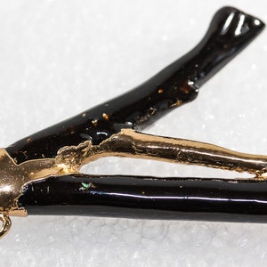 May include: A black and gold pendant with a unique branch-like design. The pendant has a gold-plated finish and a black enamel coating. It features a small loop at the top for attaching a chain.