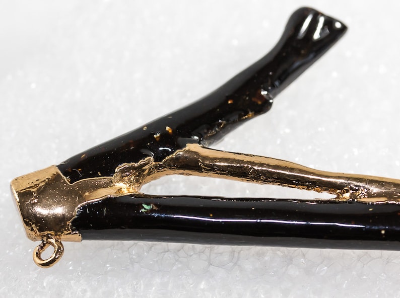May include: A black and gold pendant with a unique branch-like design. The pendant has a gold-plated finish and a black enamel coating. It features a small loop at the top for attaching a chain.
