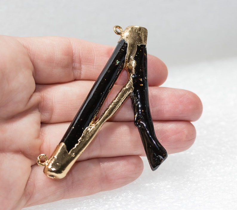 May include: A gold and black letter A pendant charm. The letter is made of a black material with gold accents. The pendant has two loops for attaching to a chain or bracelet.