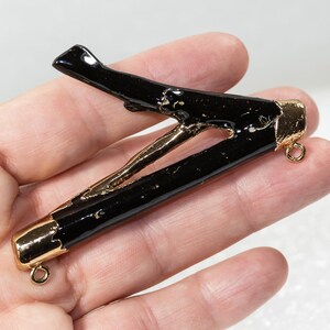 May include: Black resin branch pendant with gold accents and two jump rings. The branch is shaped like a letter V.