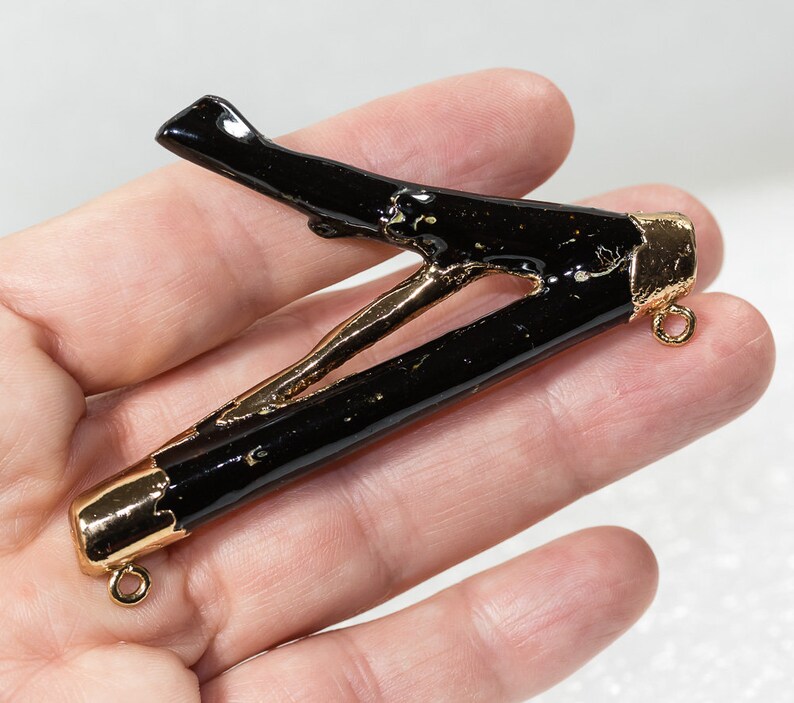 May include: Black resin branch pendant with gold accents and two jump rings. The branch is shaped like a letter V.