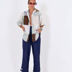 Könnte beinhalten: Ein Patchwork-Hemd in neutralen Tönen von Weiß, Beige, Braun und Hellblau, kombiniert mit einer marineblauen Hose. Das Hemd hat kurze Ärmel und einen Kragen. Die Hose ist weit geschnitten. Die Person trägt eine Sonnenbrille.