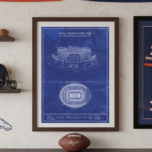 Peut inclure: Une impression d'art encadrée style plan technique présentant un dessin au trait blanc du Bronco Stadium at Mile High sur fond bleu. L'impression comprend une vue de profil et une vue aérienne du stade, avec du texte précisant le lieu.