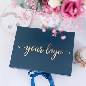 May include: A rectangular navy blue gift box featuring the text "your logo" in metallic gold script lettering on the lid. The box is secured with a matching navy blue satin ribbon tied in a bow at the bottom center, creating a clean and professional presentation.