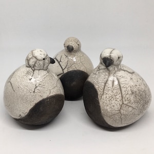 Può includere: Tre statuine di uccelli in ceramica con una glassa bianca craquelé e accenti neri. Gli uccelli sono rotondi e hanno un design semplice.