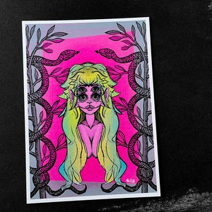 May include: A vibrant art print featuring a stylized illustration of a figure with multiple eyes, long flowing hair, and a pink complexion. The artwork is framed by two snakes and branches against a bright pink and gray background. The artist's signature is visible.