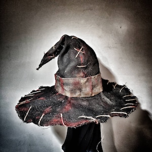 May include: A black and red witch hat with a wide brim and a pointed crown. The hat is made of a textured fabric and has a frayed edge.