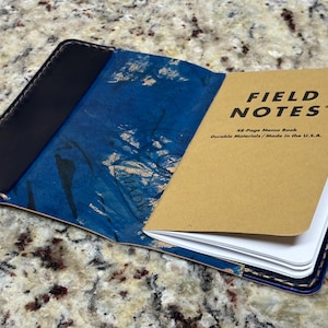 May include: Open leather notebook cover with a blue and white marbled design. The notebook is open to reveal a Field Notes memo book with the text "FIELD NOTES" and "48-Page Memo Book Durable Materials / Made in the U.S.A."