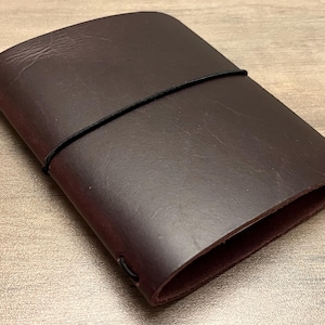 May include: A dark brown leather notebook cover with a black elastic band closure.