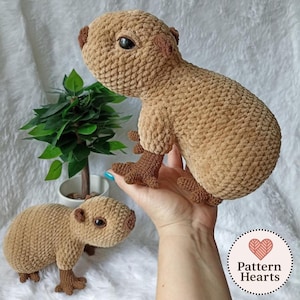 Peut inclure: Deux peluches capybara crochetées à la main, réalisées en fil marron clair doux avec des accents marron foncé sur les pattes et les oreilles. Chaque peluche présente des yeux ronds en plastique noir et un motif de mailles bouclées.