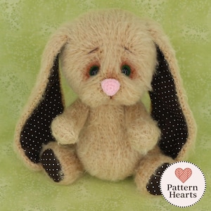 May include: A plush, tan-colored bunny with long ears and a pink nose. The inner ears and foot pads are dark brown with white polka dots. The bunny has green eyes and is sitting on a green background. A heart-shaped logo with the text "Pattern Hearts" is in the bottom right corner.