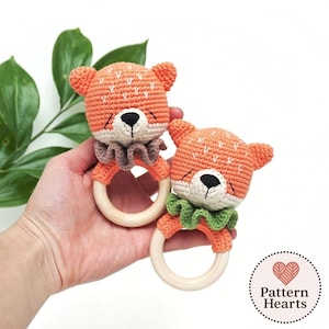 May include: Two handmade crochet fox rattles. The rattles are orange with white accents, black eyes, and a wooden ring. One has a brown ruffle, the other a green ruffle. The rattles are designed for babies and young children.