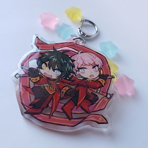 Puede incluir: Un llavero de acr&iacute;lico transparente con dos personajes de anime en estilo chibi. Los personajes llevan atuendos rojos y dorados con un dise&ntilde;o de cinta rosa y dorada. El llavero tiene un anillo de metal plateado.