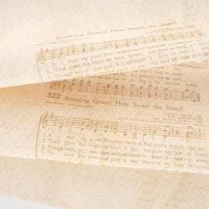 May include: A light beige fabric featuring a repeating brown print of the hymn Amazing Grace. The design includes musical notation, lyrics, and the title 322 Amazing Grace! How Sweet the Sound, layered over a faint, cursive script background pattern.