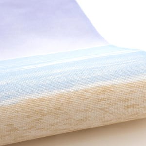 Op de afbeelding: Een rol behang met een blauw en beige gestreept patroon. Het behang heeft een textuur en is ontworpen om eruit te zien als een strandscène.