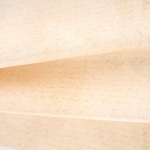 Peut inclure: Un tissu beige clair présentant un motif répétitif d'écriture cursive pâle à l'encre brune. Le matériau possède une texture tissée visible et est plié en trois couches distinctes, affichant l'écriture sur toute la surface.