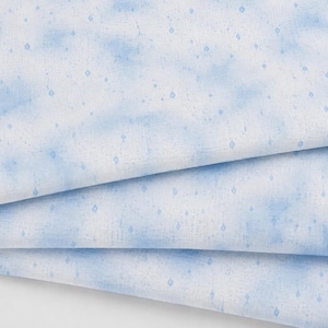 May include: A white fabric featuring a soft, watercolor-style blue cloud pattern with small, evenly spaced blue diamond-shaped accents. The textile is folded into three distinct layers, showcasing the repeating print and the woven texture.