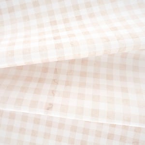 May include: A folded piece of fabric featuring a light beige and white gingham check pattern. The textile displays a consistent grid design with soft, muted tones and a woven texture visible across the surface of the layered material.