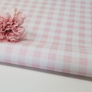 May include: Pink and white gingham fabric, folded, with two carnation flowers. The fabric has a classic checkered pattern, ideal for tablecloths or craft projects. The flowers are a light pink and white.