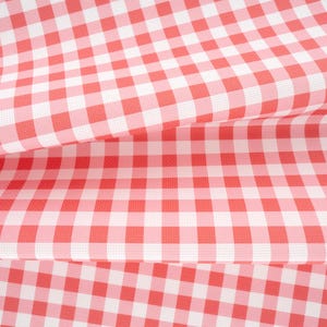 May include: A fabric featuring a classic gingham pattern with alternating squares of vibrant red and crisp white. The material is folded in layers, showcasing the consistent checkered design and the woven texture of the textile surface throughout.