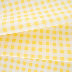 May include: A fabric featuring a classic yellow and white gingham check pattern. The material is folded in layers, displaying the consistent grid design of small, alternating yellow and white squares across the entire surface of the textile.