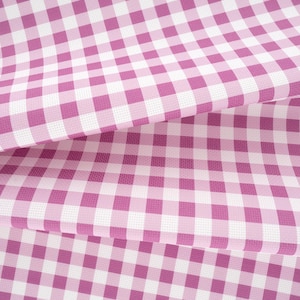 May include: A fabric featuring a classic gingham pattern with alternating squares of magenta pink and white. The material is folded in layers, showcasing the consistent checkered design and the woven texture of the textile surface throughout.