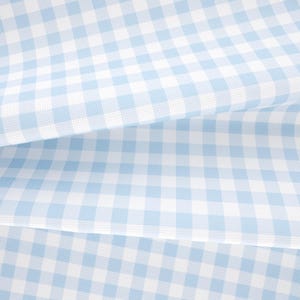 May include: A light blue and white gingham fabric featuring a classic checkered pattern. The material is folded into multiple layers, creating soft, flowing drapes that highlight the consistent grid design across the textile surface.
